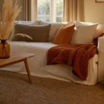 Cozy fall living room decor with a cream sofa, rust chunky knit throw, layered pillows and warm candlelight