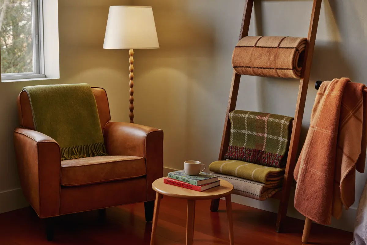 A fall reading corner with a leather armchair, olive throw, warm floor lamp and blanket ladder
