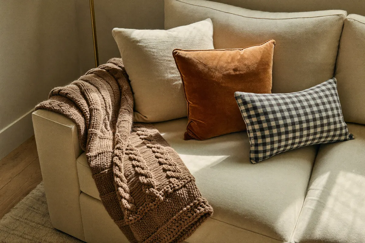 Chunky caramel knit throw and rust pillows on a cream sofa in soft window light