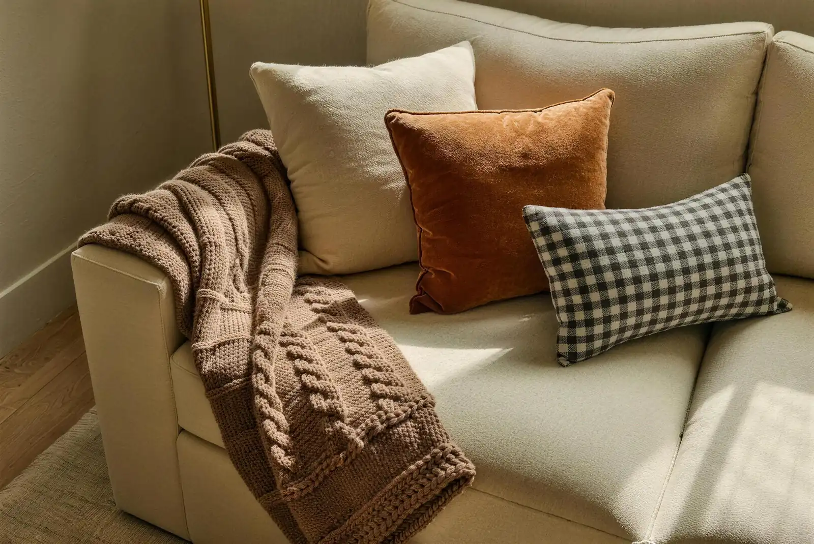 Chunky caramel cable-knit throw and rust velvet pillow styled on a cream linen sofa
